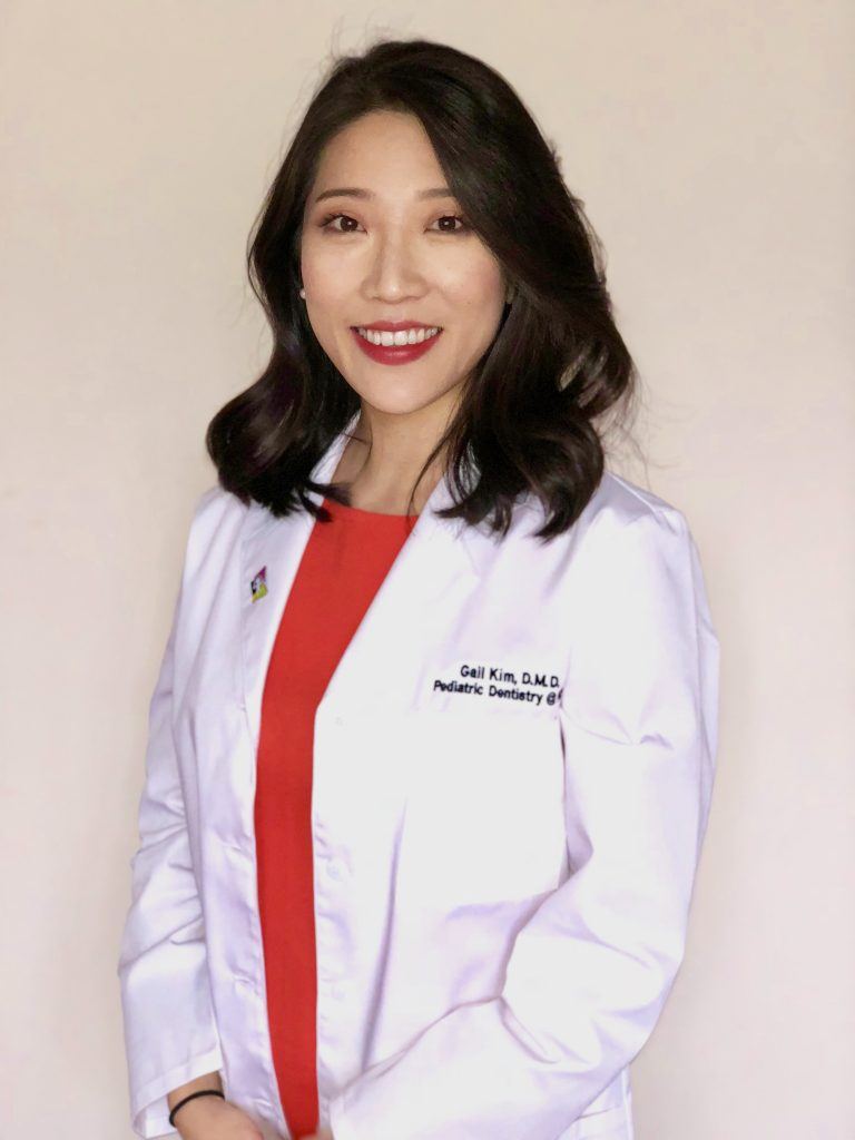 Dr. Kim smiles while in a white doctor's coat over a red shirt.